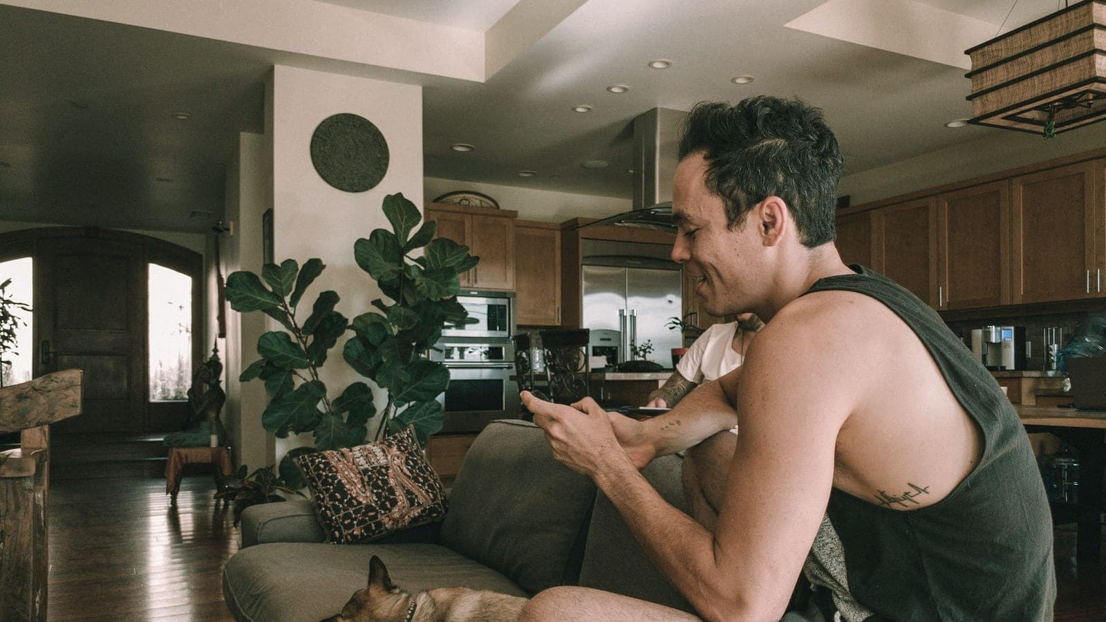Man scrolling on his phone on a living room couch with his dog beside him
