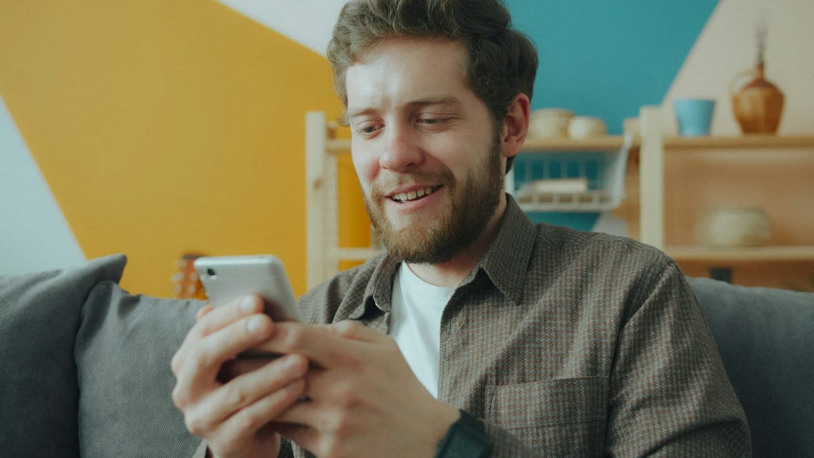 Bearded man on a couch smiling at a message on his phone
